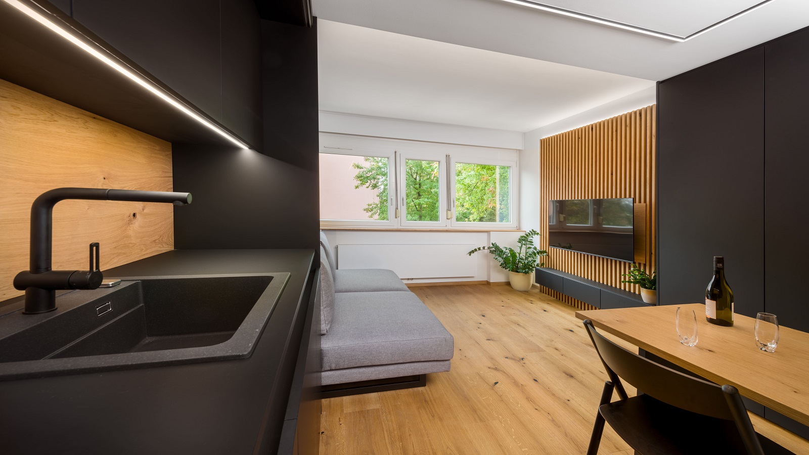 Kitchen and dining room interior with black furniture, next to the living room with wooden elements