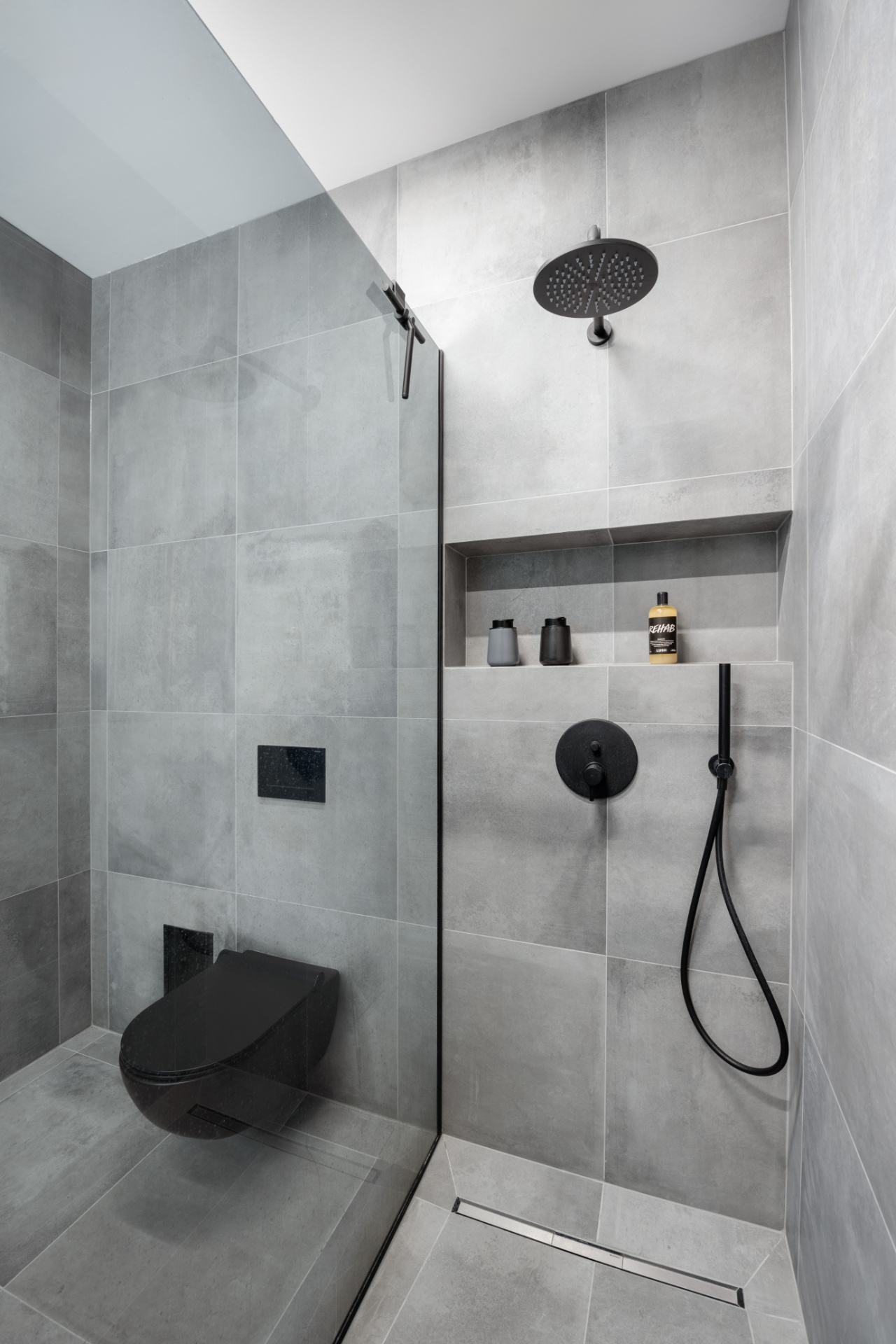 Bathroom interior with grey tiling, a black toilet and a black shower