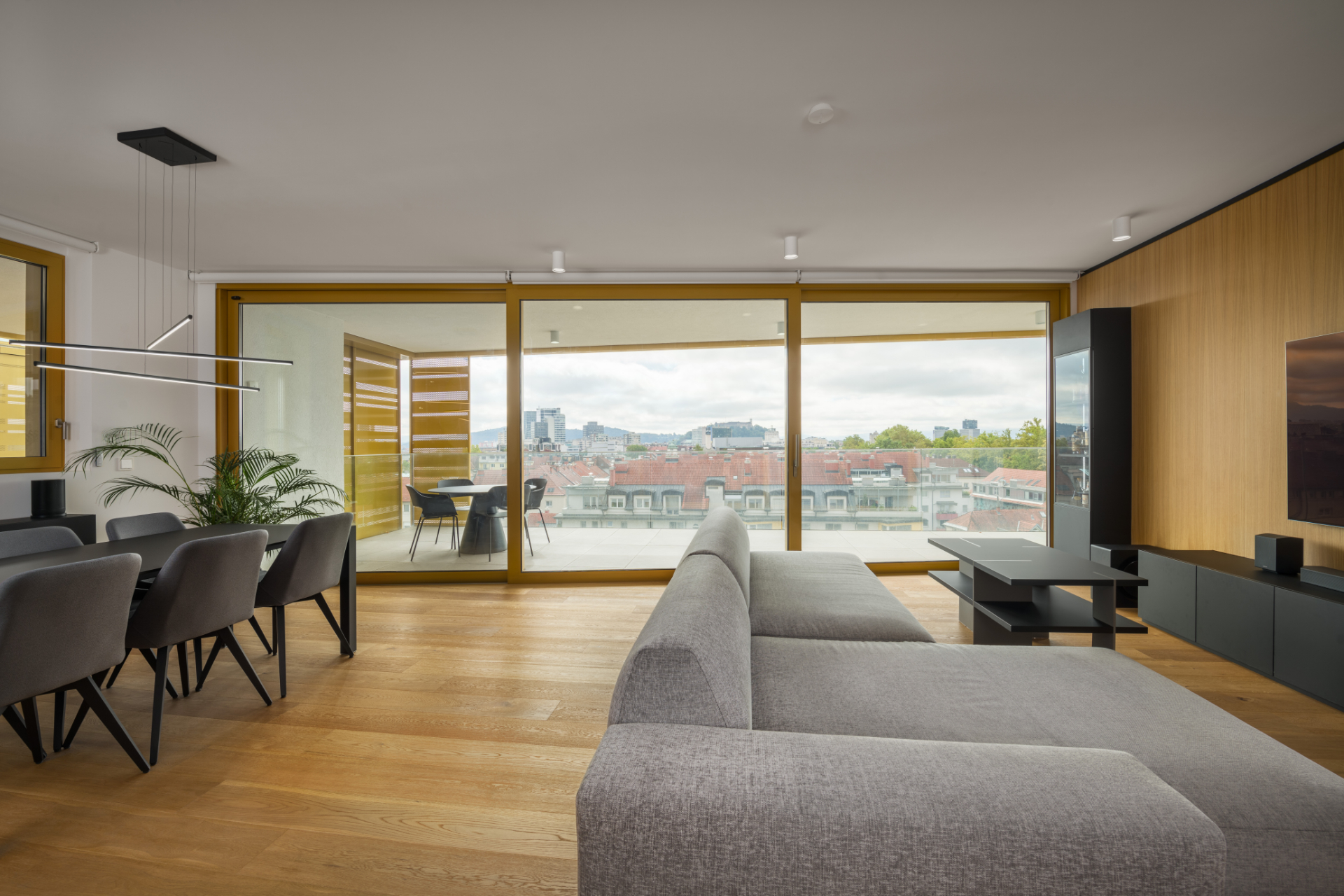Modern living room interior with a panoramic window, a black dining table, a grey sofa and a balcony