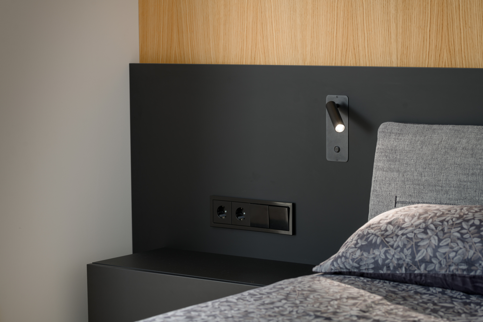 Detail of a wall covering with an integrated light and sockets next to the bed