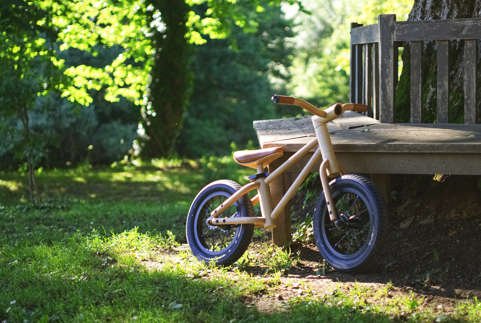 Wooden balance bike next to a bench in the park as an example of sustainable industrial design