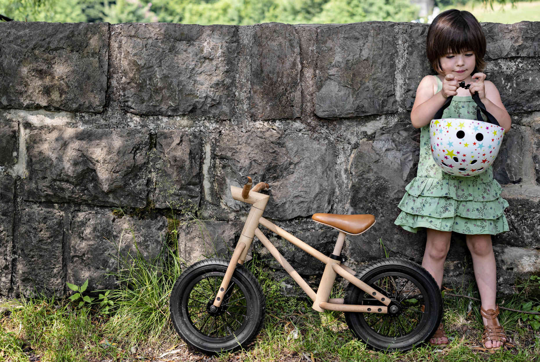 A child with the woode Bixie balance bike in nature next to a small wall made of stone