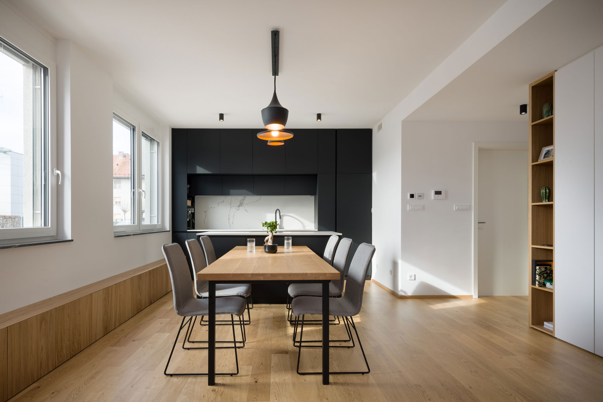 Lesena kuhinja z veliko jedilnico, kuhinjskim otokom in naravno svetlobo v minimalističnem interierju