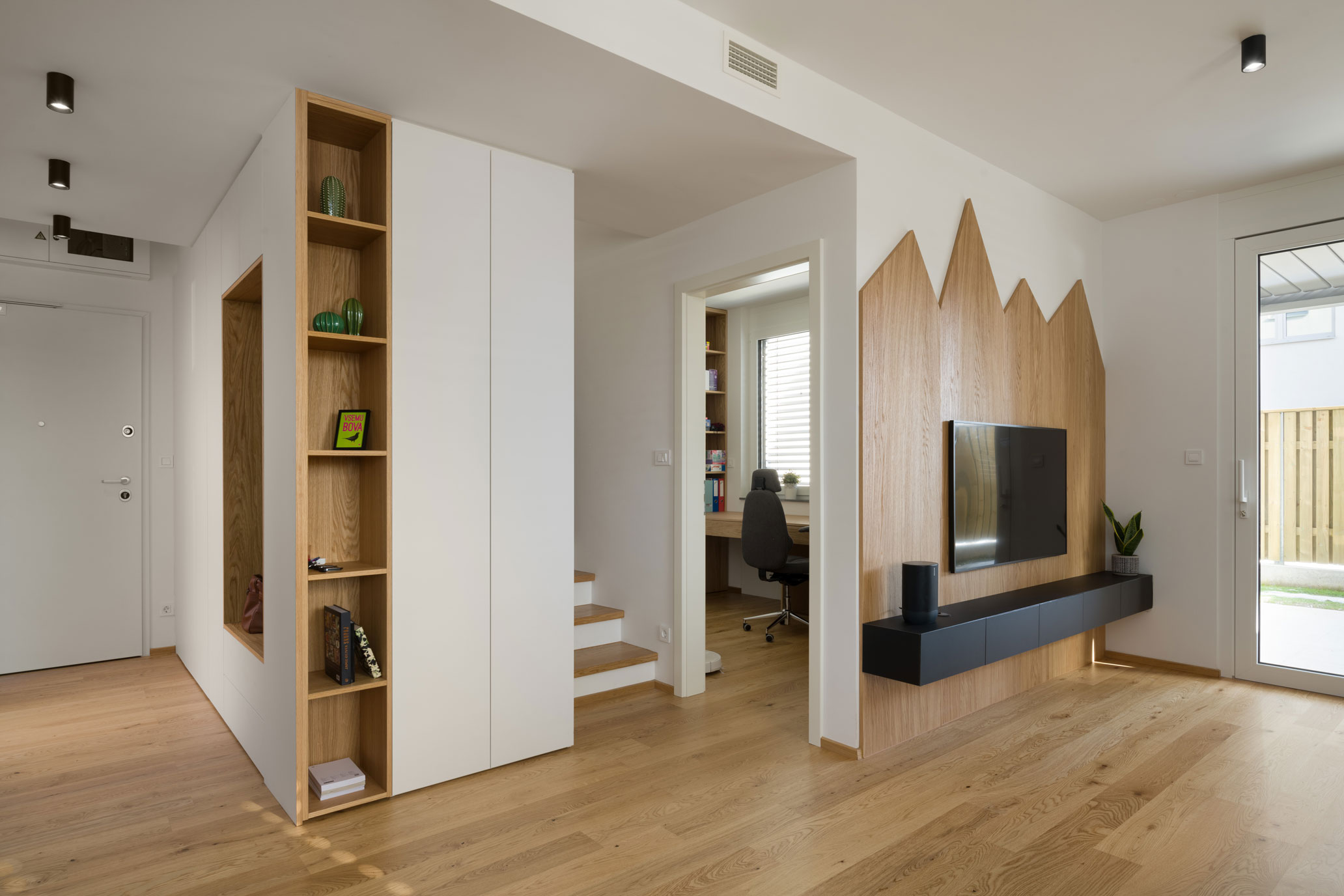 Living room with a TV mounted on decorative wood, a cabinet and a passage to the office