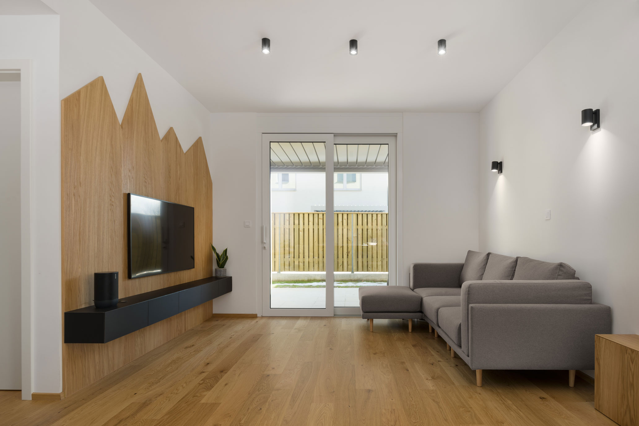 Dnevna soba s kavčem, teraso in stensko nameščeno televizijo na leseni nastavek v obliki gora