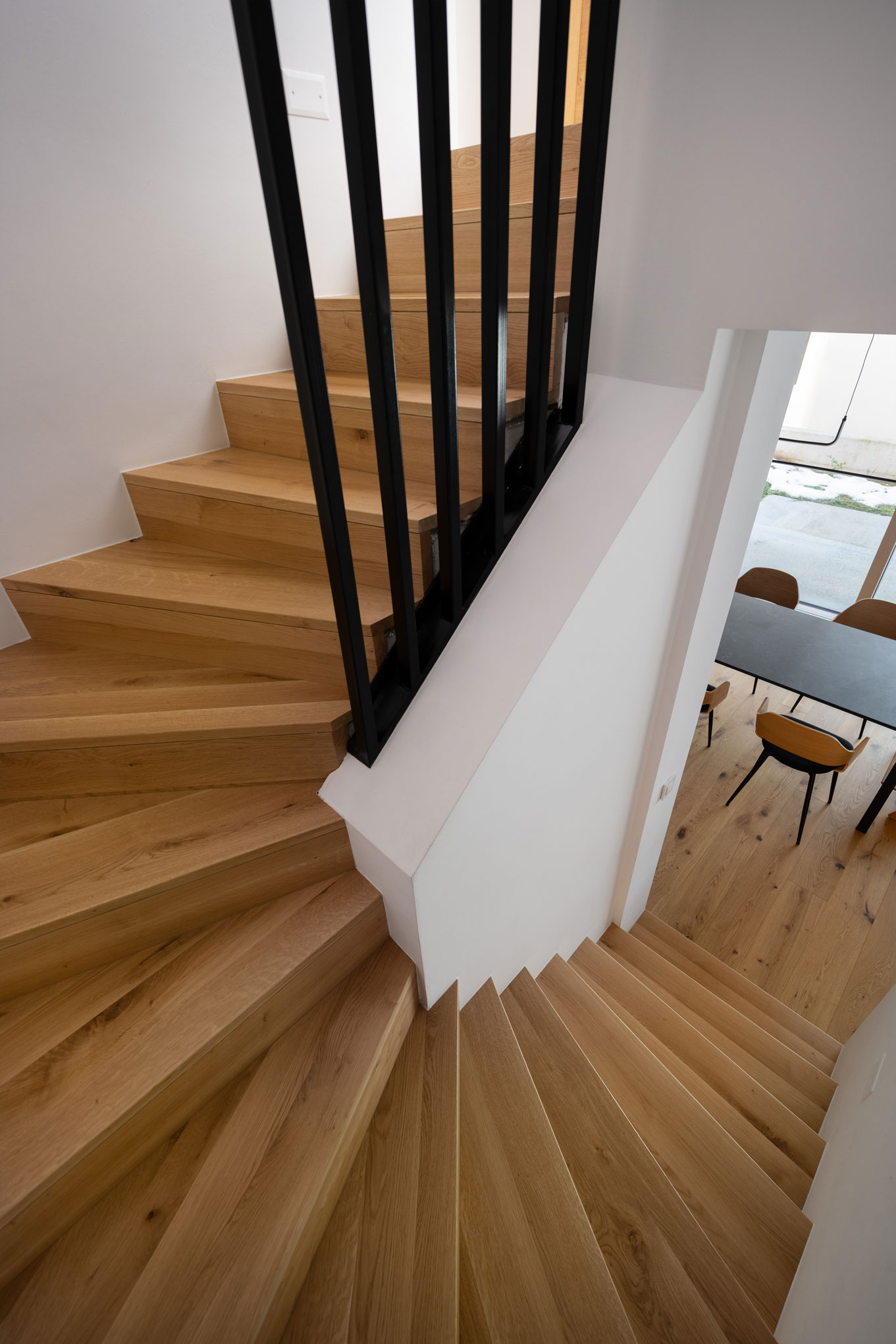 Curving wooden staircase with black metal railings, work of an interior designer