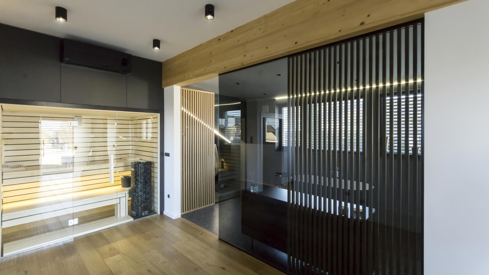 Lesena savna s steklenimi vrati zraven temne kopalnice z banjo in omaro