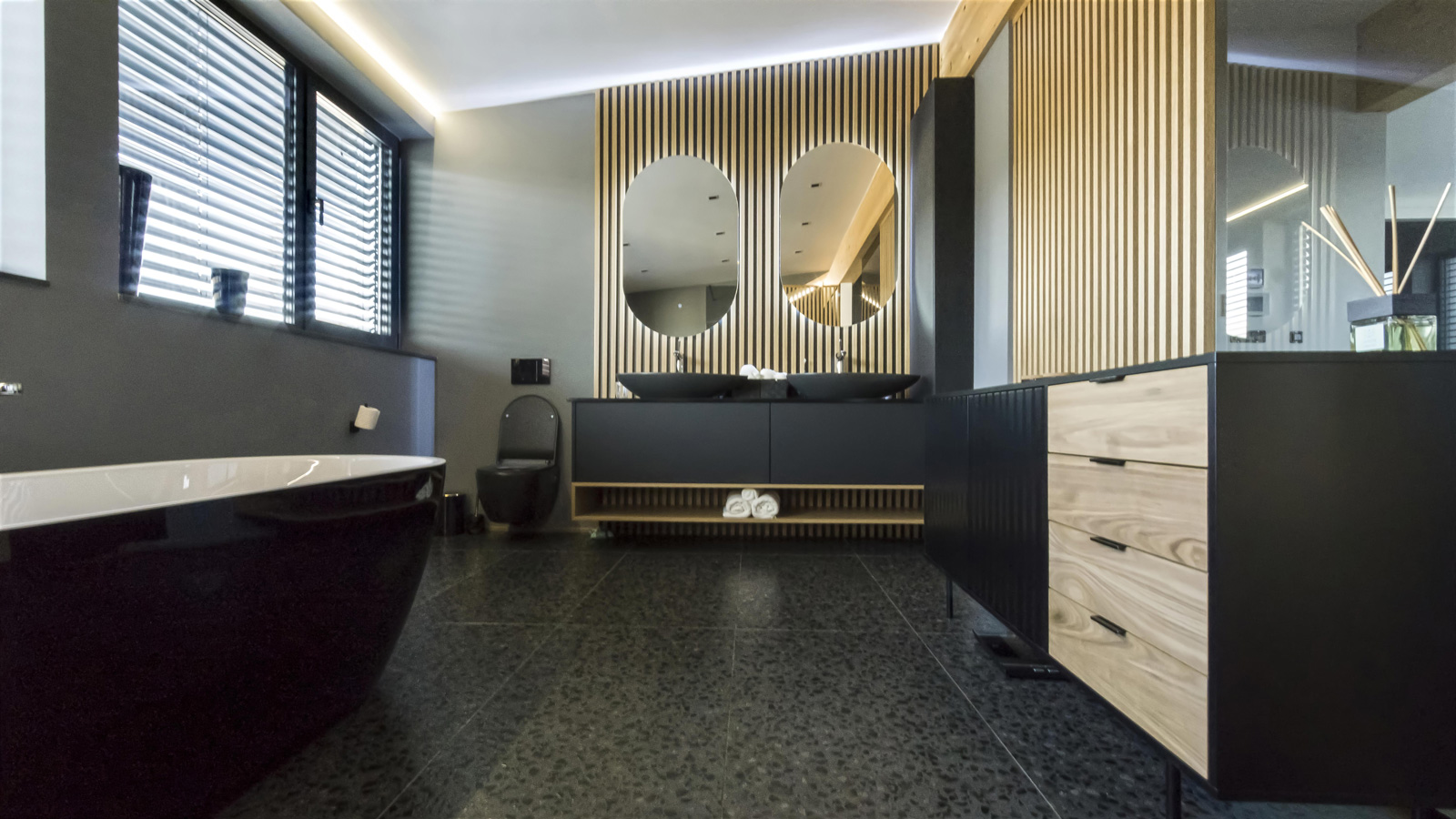 Moderna kopalnica z lesenimi elementi, umivalnikoma in črno kadjo, ki ustvarijo sodoben videz notranjega oblikovanja