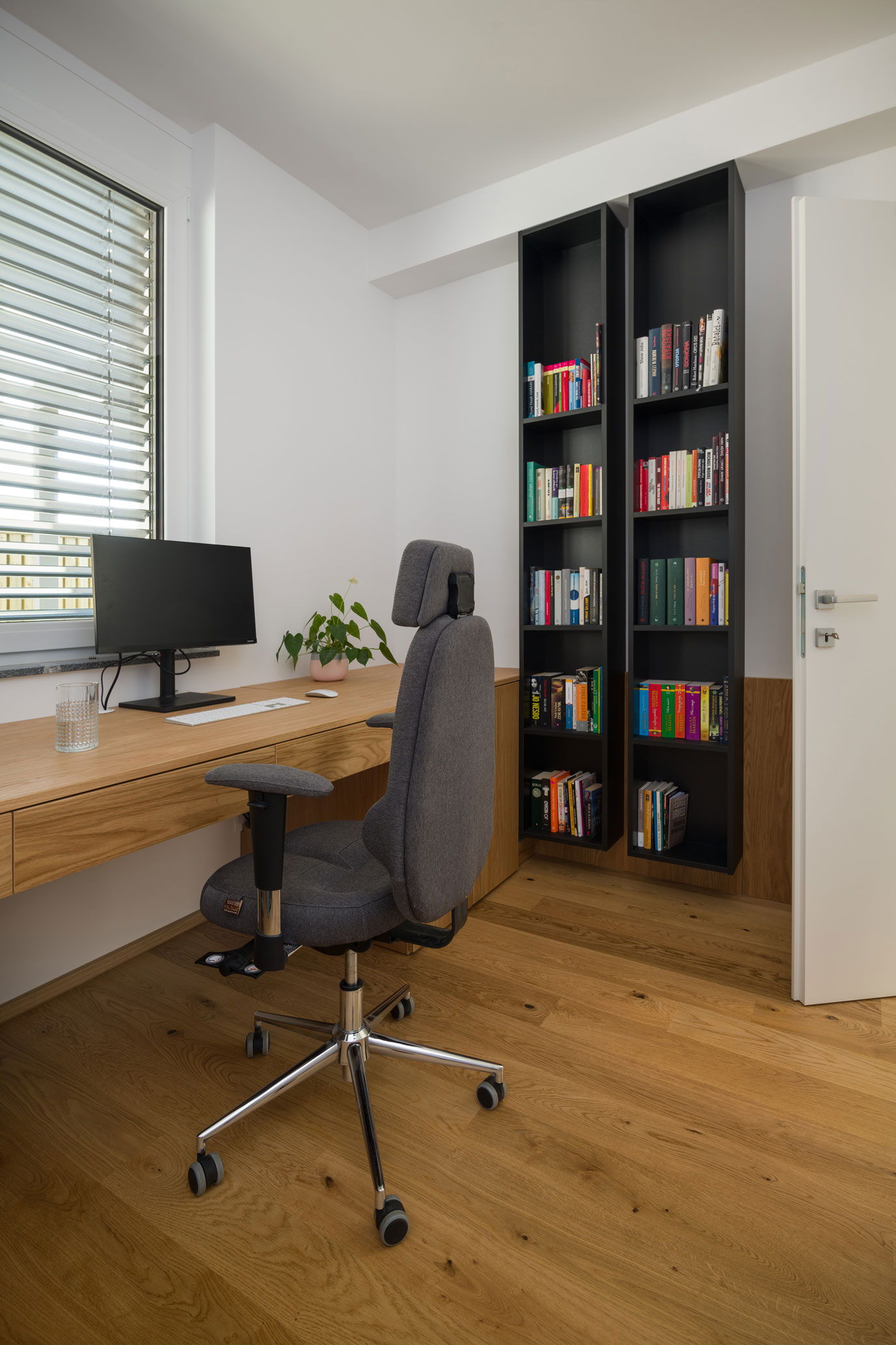 Delovni prostor s pisalno mizo, stolom in črno omaro za knjige, delo notranjega oblikovalca