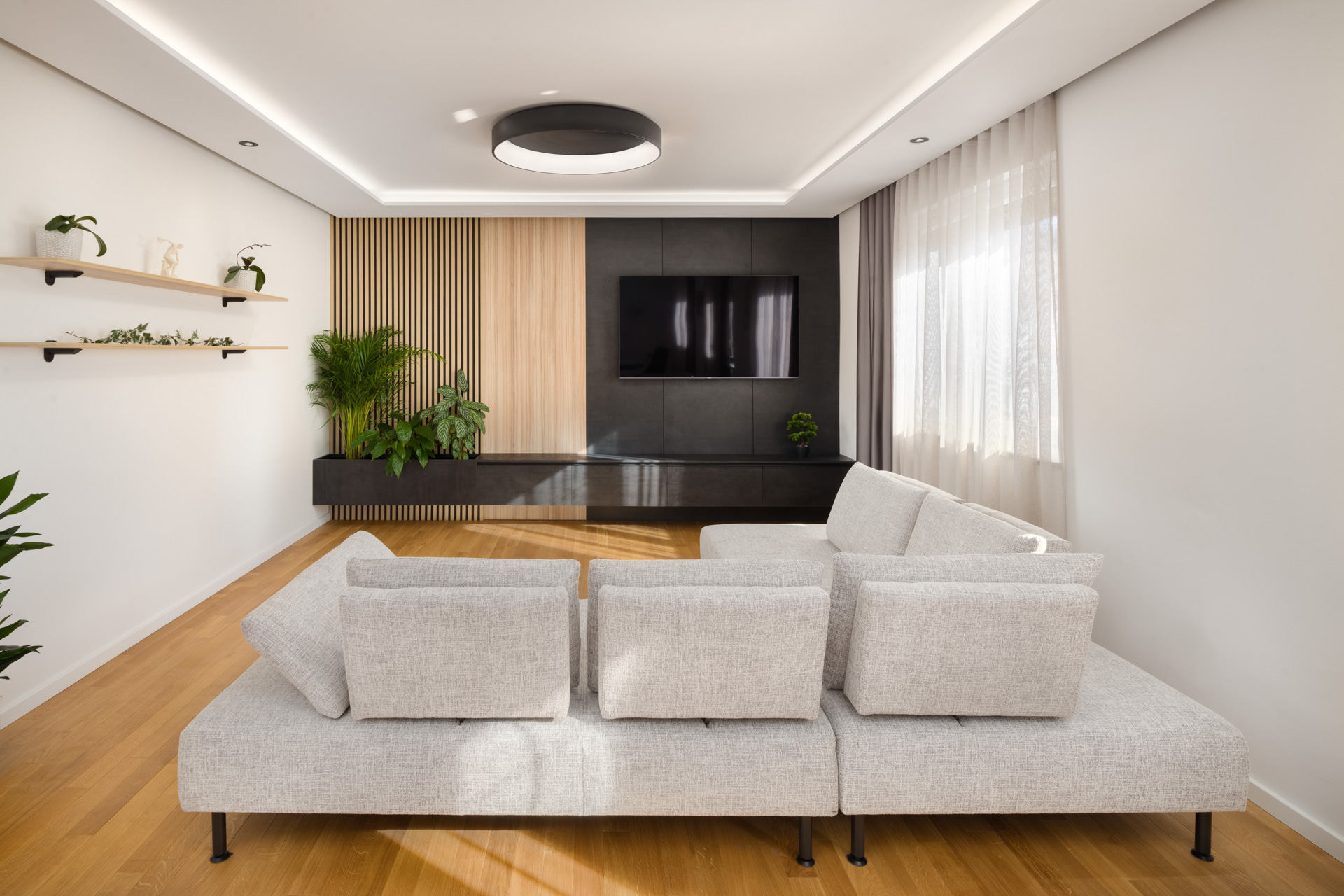 Bright livingroom with wooden floors, white walls, a white sofa and a wall-mounted TV