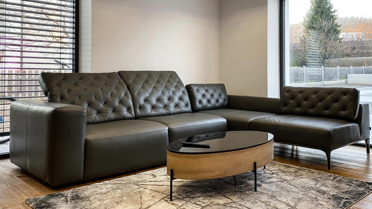 Livingroom with plenty of natural light and a black sofa next to a wooden coffee table.