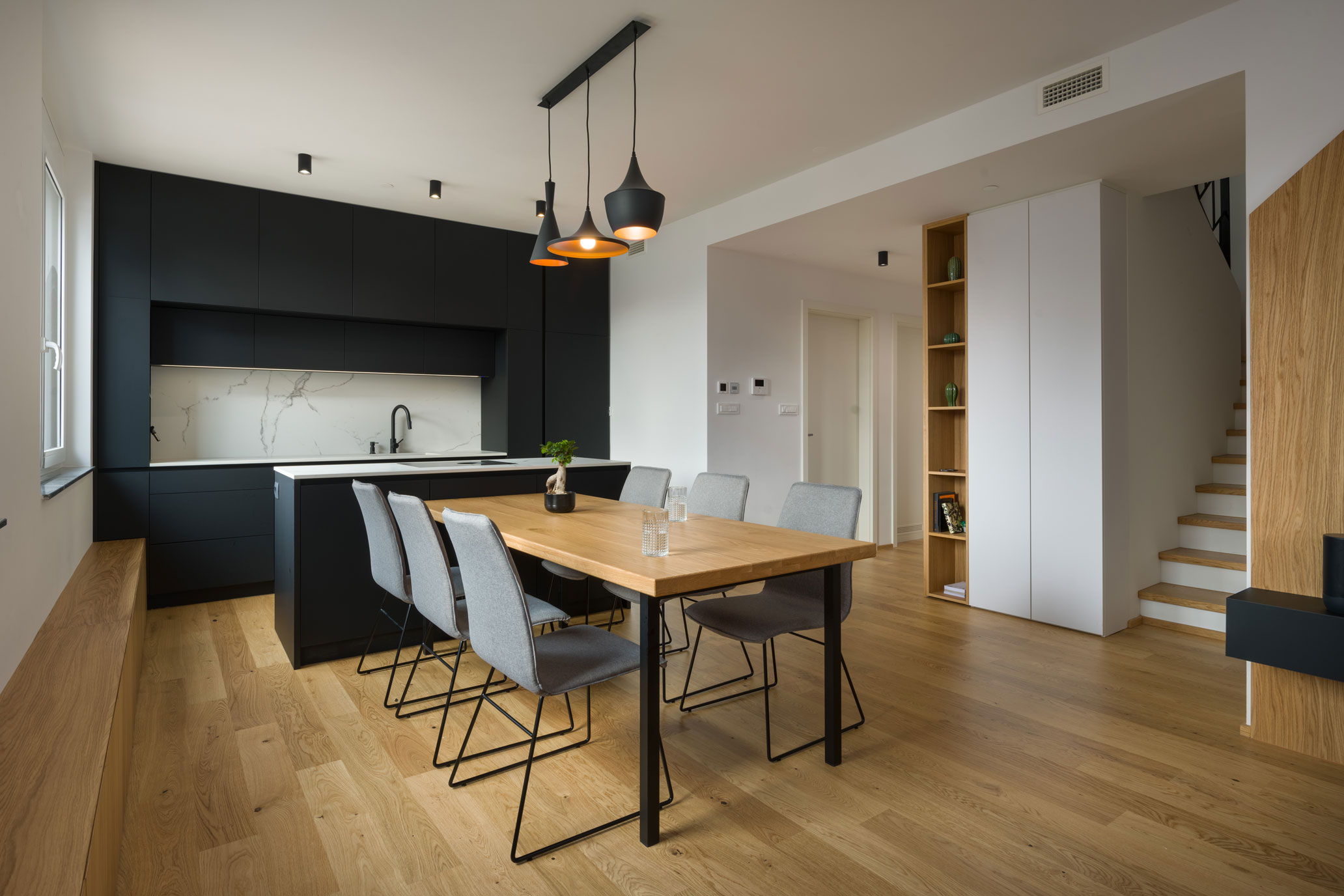 Dining room with wooden floors and a dining table next to the kitchen with a kitchen island and natural light.