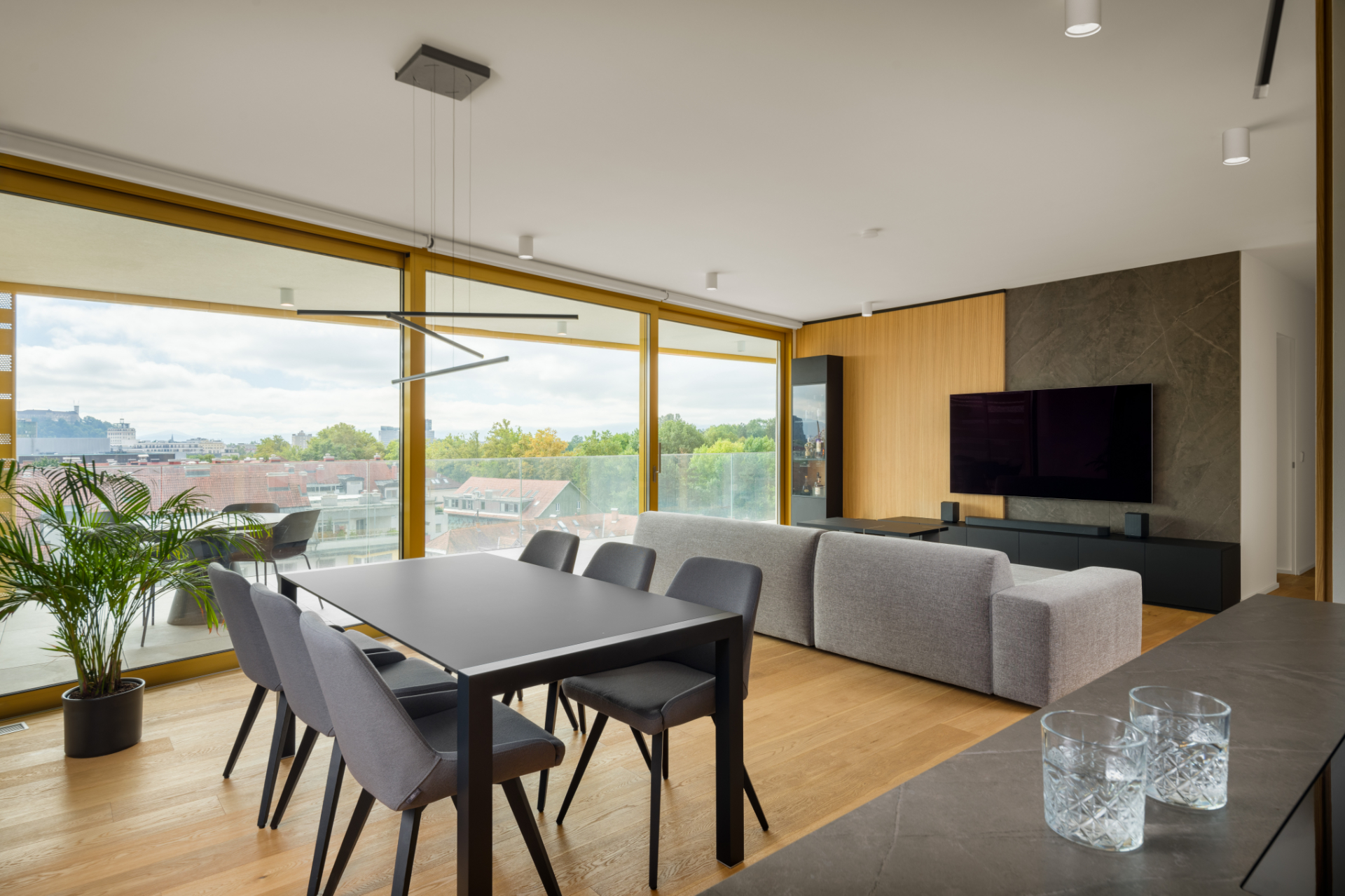 Bright livingroom with wooden floors, a gray sofa, a black dining table and a wall-mounted TV.