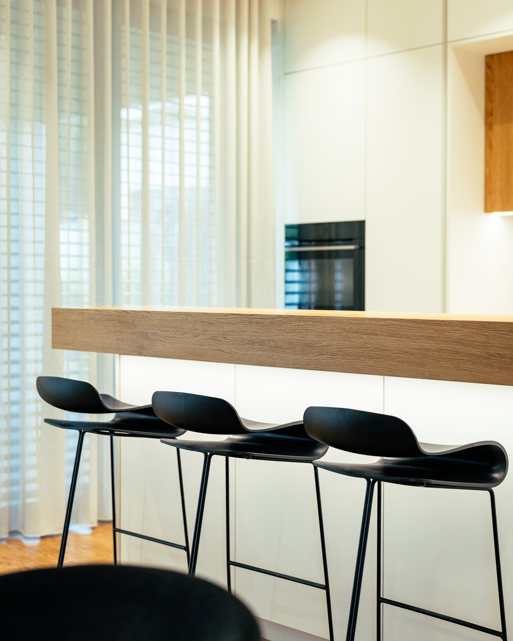 Kuhinjski otok z lesenim pultom in tremi, črnimi barskimi stoli