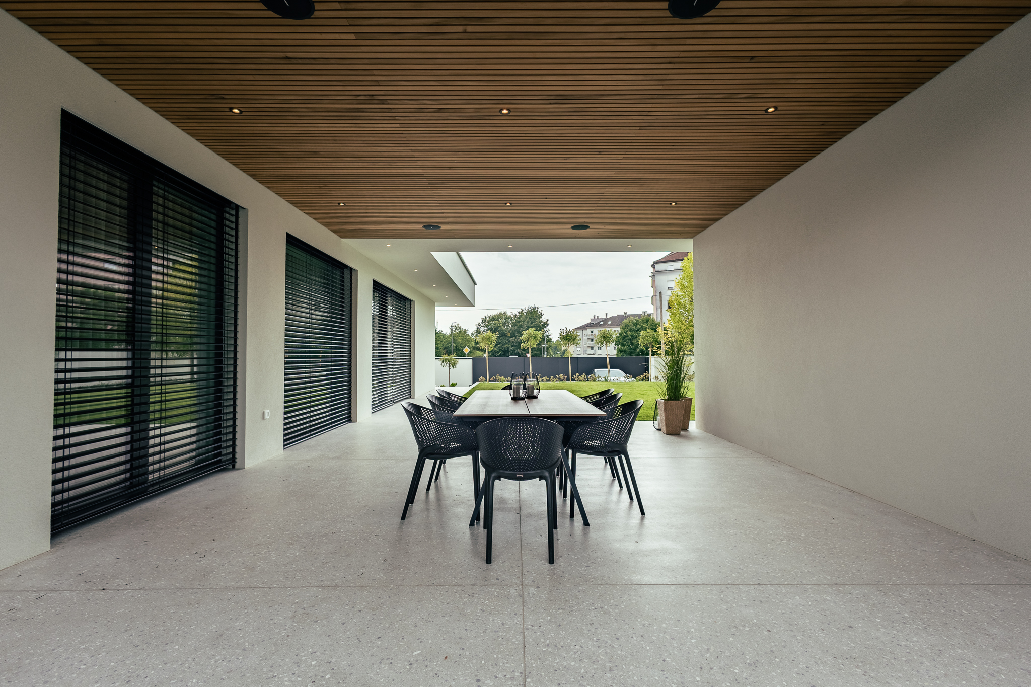 Terasa v luksuzni vili, z vrtom v ozadju in jedilno mizo okoli katere so postavljeni črni stoli